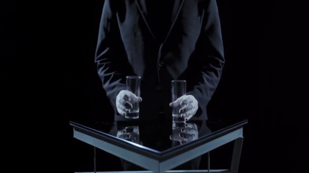 Male hands on a dark background with empty glasses make transfusion movements of an invisible liquid. Dark background. Illusion. Imaginary. - Metraje, vídeo