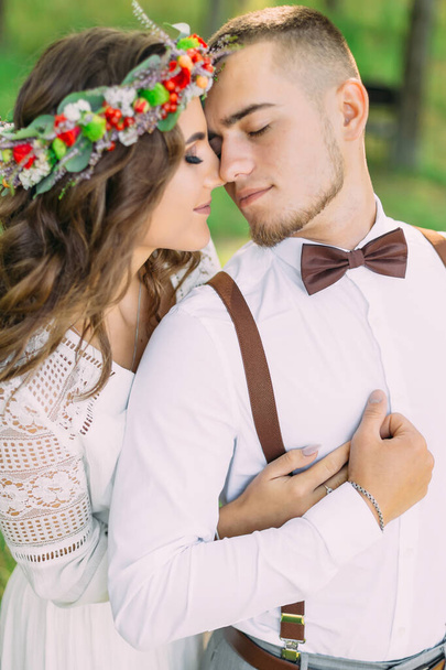 girl in a wreath hugged the guy from back side and they closed their eyes. guy in a white shirt with bow tie and suspenders  - 写真・画像
