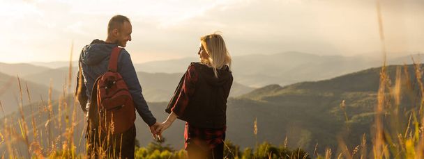 Happy traveler young couple resting in the mountains at sunset in spring or summer season - Foto, imagen