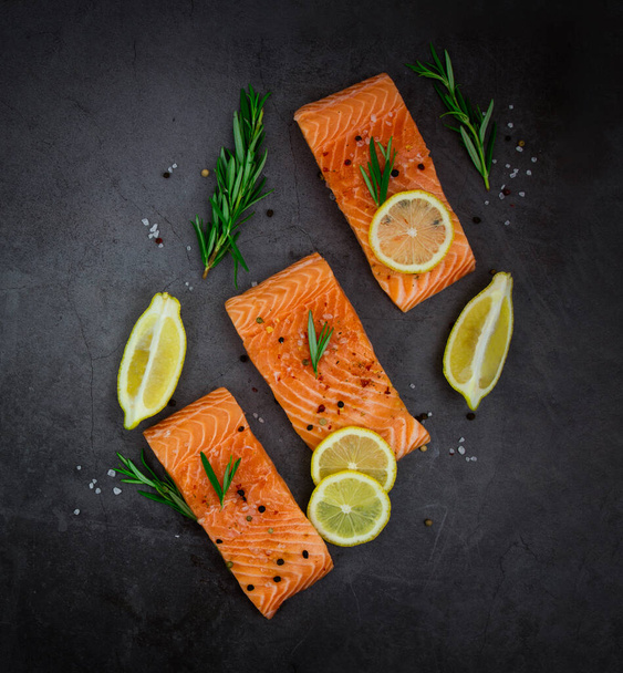 Salmon fillet steaks with lemon and herbs on a black background. - 写真・画像