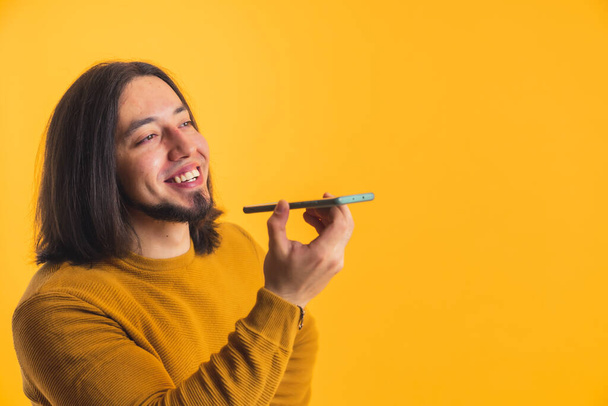 A happy long haired person on a yellow and orange background talking to a mobile phone listening in a room. High quality photo - Photo, Image