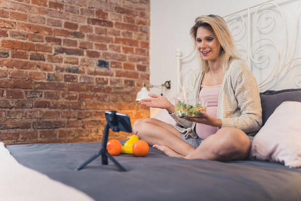 Millennial caucasian influencer blonde woman sharing her pregnancy advice with her followers during livestream via smartphone. Salad. Healthy eating. High quality photo - Fotografie, Obrázek