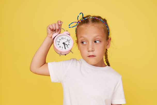 Portrait of a cute girl with a small alarm clock on a yellow background - Foto, afbeelding