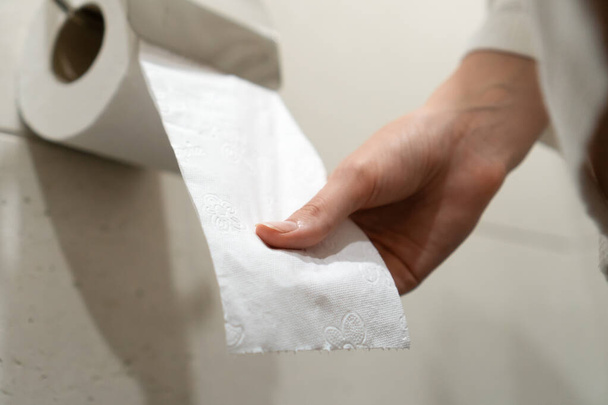 Жінка в білому пальто сидить на туалеті і тягне туалетний папір у ванну кімнату. Вибірковий фокус
 - Фото, зображення