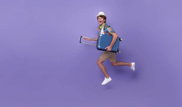 Excited happy young man tourist with luggage jumping isolated on purple studio background. - Valokuva, kuva