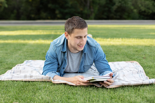 Молодий чоловік розслабляється і читає книгу, лежачи на газоні. Щасливий чоловік лежить на зеленій траві і віддалено вчиться. Дорослий студент читає в парку. Насолоджуйся студентським життям. усміхнений чоловік працює на відкритому повітрі
 - Фото, зображення