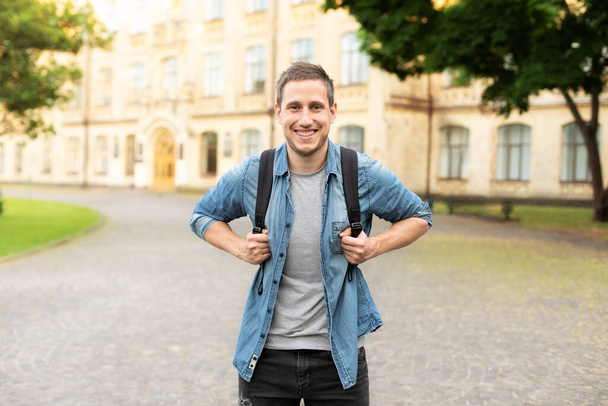 Улыбающийся студент университета с рюкзаком прогулка по университетскому кампусу, концепция образования. Портрет счастливого красавца на улице, копия пространства. человек, гуляющий в парке летом - Фото, изображение
