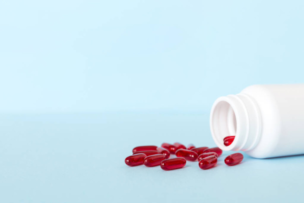 Red pills spilled around a pill bottle. Medicines and prescription pills flat lay background. Red medical capsules. - Photo, Image