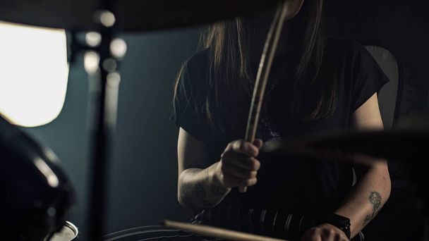 Young female drummer with spectacles plays a drum set holding drumstick in hands - 写真・画像