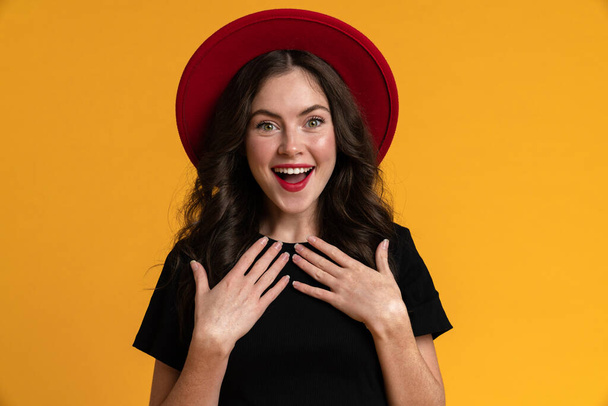 White young woman in red hat smiling while looking at camera isolated over yellow background - Foto, imagen