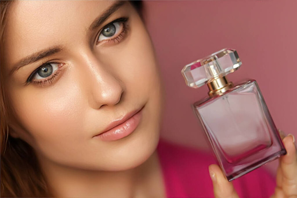 Άρωμα, προϊόν ομορφιάς και καλλυντικά μοντέλο προσωπογραφία σε ροζ φόντο, όμορφη γυναίκα κρατώντας μπουκάλι άρωμα με λουλουδάτο θηλυκό άρωμα, μόδα και μακιγιάζ έννοια - Φωτογραφία, εικόνα