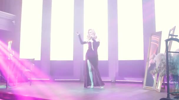 Blond woman singer with microphone on stage with spotlights and looks straight into the frame. Lady in burgundy dress with rhinestones sings - Filmati, video