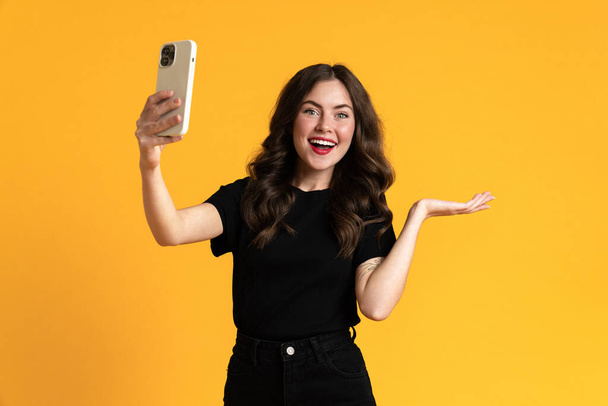 White woman holding copyspace while taking selfie on cellphone isolated over yellow background - Foto, Bild