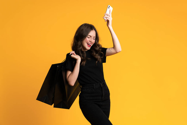 White young woman posing with shopping bags and cellphone isolated over yellow background - Fotoğraf, Görsel
