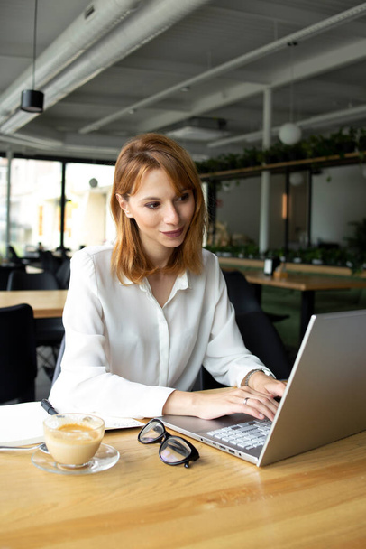Geschäftsfrau tippt im weißen Hemd mit Brille am Tisch in den Laptop - Foto, Bild