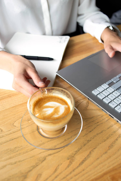 Beautiful business woman making notes with a pen with a cup of coffee on the foreground - Photo, image