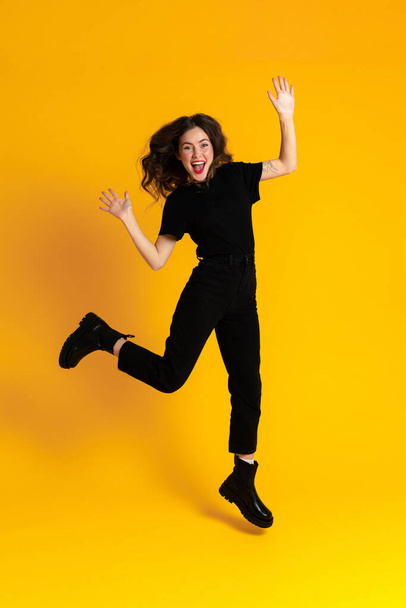 White excited woman in black t-shirt making fun and jumping isolated over yellow background - Foto, Bild