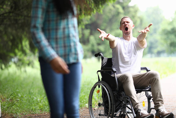 Een vrouw loopt gefrustreerd weg van een man in een rolstoel. Scheiding en scheiding met mensen met een handicap concept - Foto, afbeelding