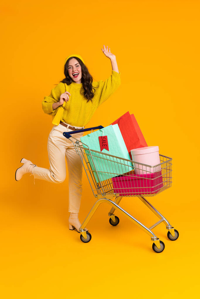 White woman making fun while posing with shopping cart isolated over yellow background - Fotó, kép