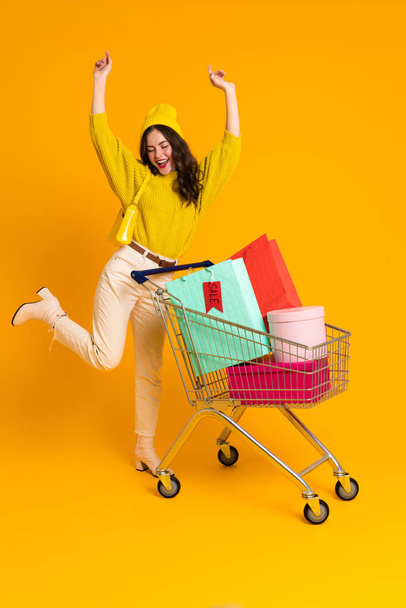 White excited woman making fun while posing with shopping cart isolated over yellow background - Foto, Imagen