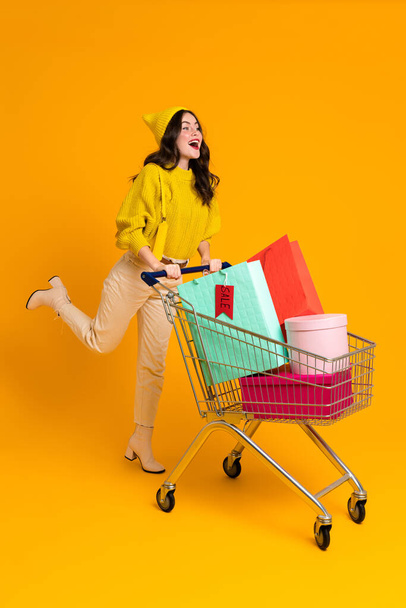 White excited woman laughing while posing with shopping cart isolated over yellow background - Фото, зображення