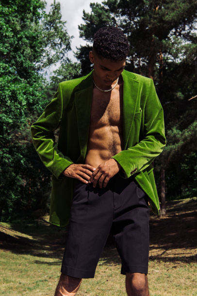 young african american man in black shorts and green blazer standing with hand on hip in forest - Foto, immagini