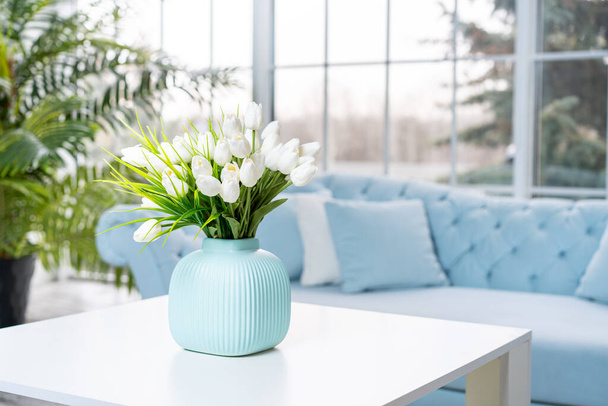 Luxury house interior. ELegant living room Modern Interior design. White Living Room Tulip flowers standing vase on coffee table With big panoramic window on background - Фото, зображення