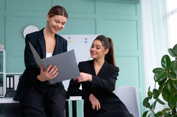 Young women leaders are checking financial statements from paper documents. Two female confident business worker dressed black suit in office checking financial document looking folder and discussing - Photo, image