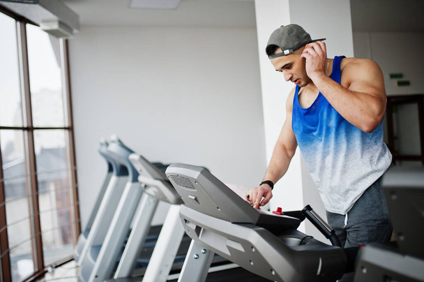 Fit and muscular arabian man running on treadmill in gym. - Foto, afbeelding