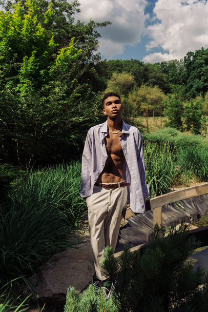 african american man in blue shirt and white trousers posing near lake in park - Foto, immagini