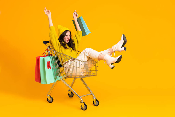 White excited woman making fun in shopping cart isolated over yellow background - Foto, immagini