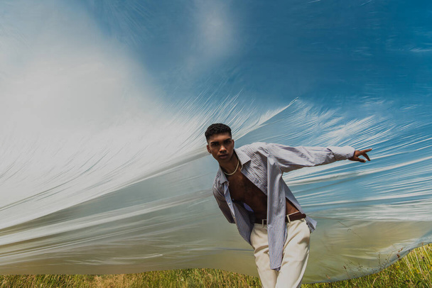 african american man in trendy clothes pointing with finger under cellophane film in field - Φωτογραφία, εικόνα