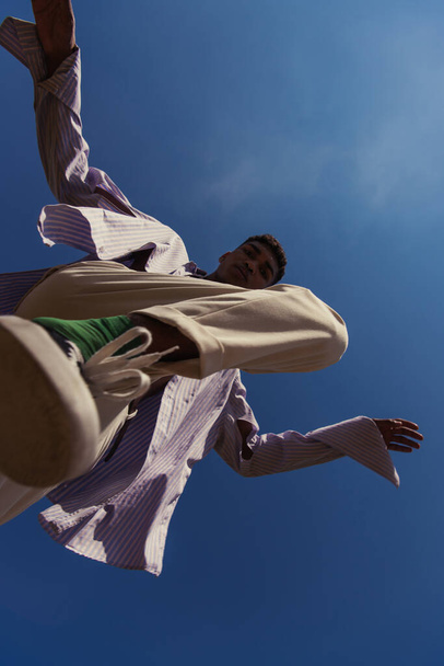 bottom view of african american man in trendy clothes under blue and clear sky - Foto, afbeelding