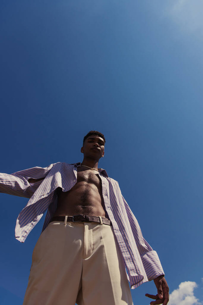 low angle view of young african american man in summer clothes under cloudless sky - Foto, imagen