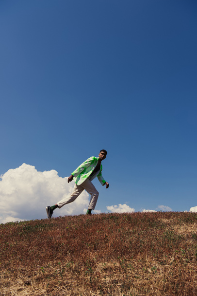 fashionable african american man running in field under blue sky with white clouds - Photo, image