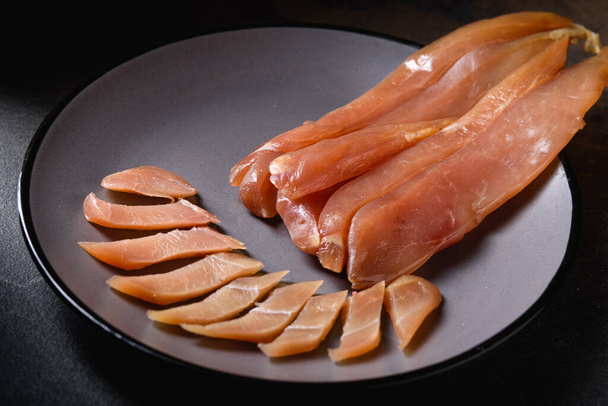 Cured Smoked Meat - raw Meat Sausage Meat. Close-up view of Delicious Sliced Chicken Basturma on Gray Plate on Dark Background. Snack for beer. Pastrami - Photo, Image