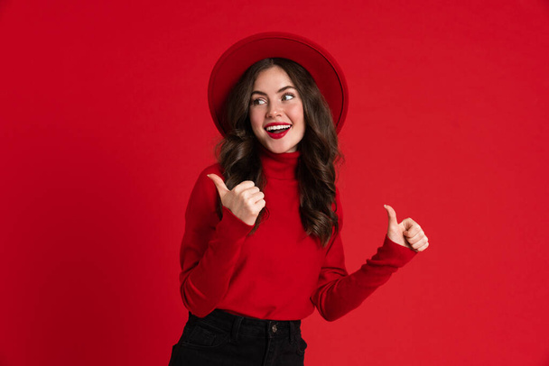 White woman wearing hat smiling and pointing finger aside isolated over red background - Zdjęcie, obraz