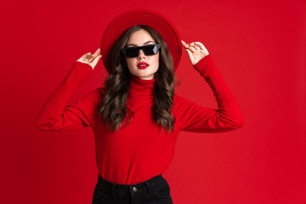 White woman in sunglasses posing and looking at camera isolated over red background - Fotografie, Obrázek