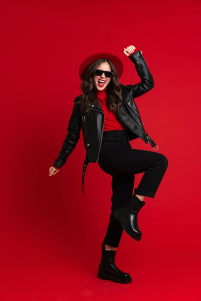 White woman in leather jacket laughing while dancing on camera isolated over red background - Fotó, kép