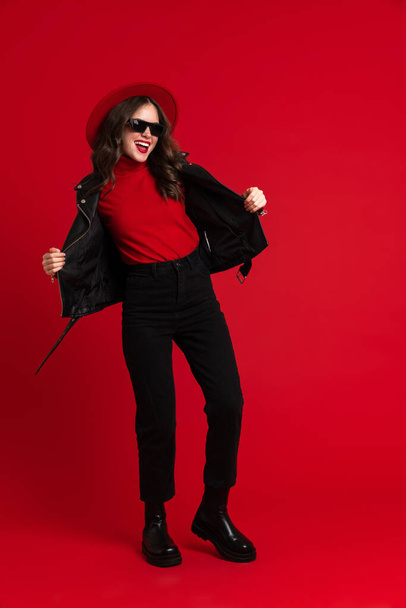 White woman in leather jacket laughing while dancing on camera isolated over red background - 写真・画像