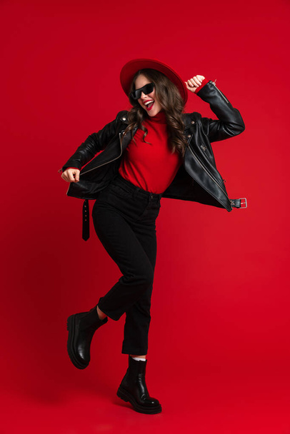 White woman in leather jacket laughing while dancing on camera isolated over red background - Foto, imagen