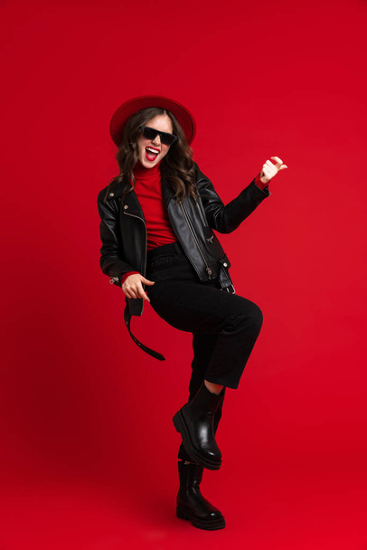White woman in leather jacket laughing while dancing on camera isolated over red background - 写真・画像