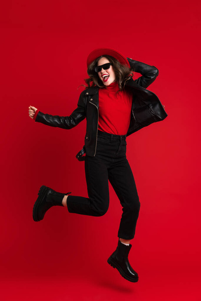 White woman in leather jacket laughing while dancing on camera isolated over red background - Foto, Imagen