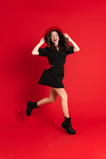 White woman wearing dress laughing while dancing on camera isolated over red background - Fotó, kép