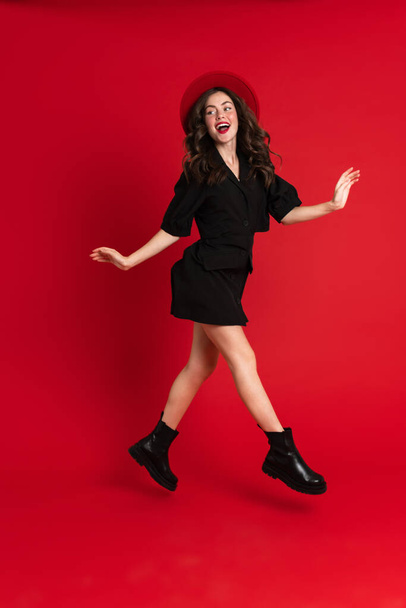 White woman wearing dress laughing while dancing on camera isolated over red background - Foto, Imagem