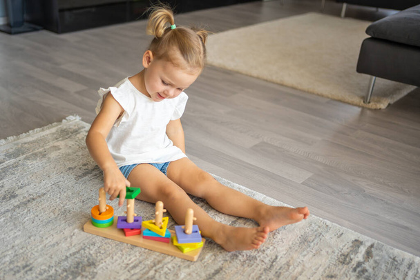 Мила біла дівчинка грає на підлозі вдома з еко-дерев'яними іграшками. Іграшка Монтессорі. Дитина грає в освітні ігри. Високоякісна фотографія
 - Фото, зображення