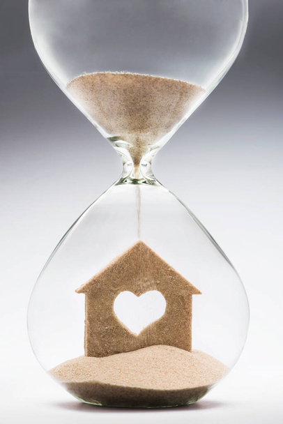 A house needs insurance with time. House care concept with falling sand taking the shape of a house inside a hourglass. - Foto, immagini