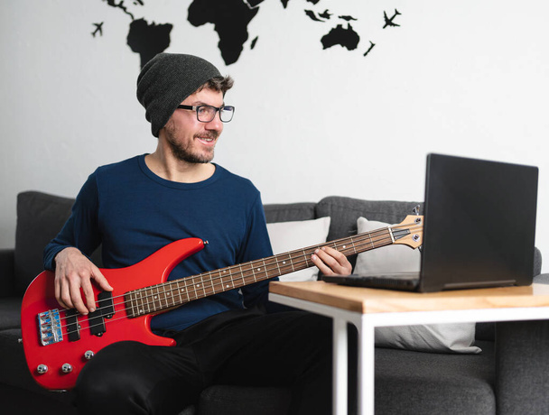 Caucasian young man learns how to play bass online with his computer - Fotó, kép