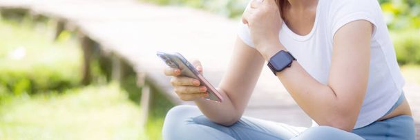 Szczęście młoda azjatycka kobieta siedzi i korzysta ze smartfona w sieci społecznościowej online w parku, relaks dziewczyny za pomocą smartfona i rozmowy wideo w lecie w ogrodzie, koncepcja komunikacji. - Zdjęcie, obraz
