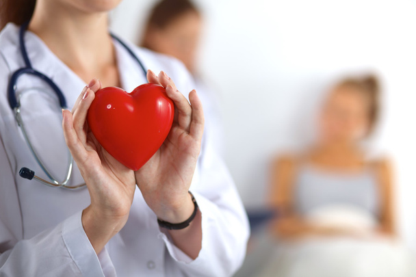 Νεαρή γυναίκα γιατρός κρατώντας μια κόκκινη καρδιά, απομονωμένη σε λευκό φόντο - Φωτογραφία, εικόνα